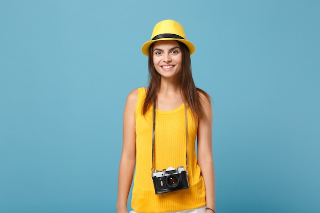 Reiziger toeristische vrouw in gele zomer casual kleding, hoed met fotocamera geïsoleerd op blauwe muur. Vrouwelijke passagier die naar het buitenland reist om in het weekend te reizen. Lucht vlucht reis concept.