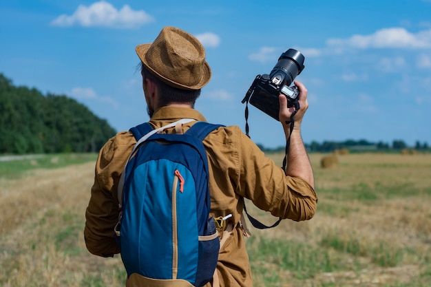 Reizigersfotograaf met een camera in zijn hand tegen de achtergrond van een veld en hooibergen.