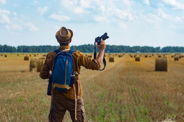 Reizigersfotograaf met een camera in zijn hand tegen de achtergrond van een veld en hooibergen