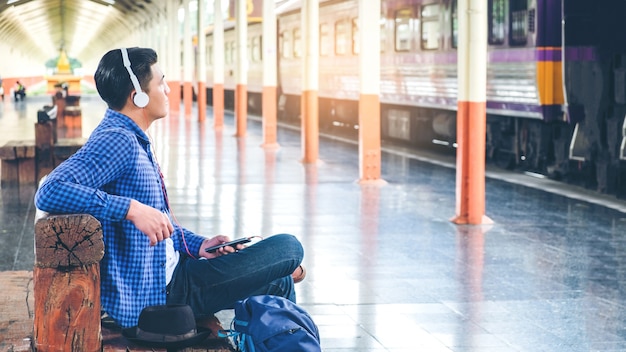 Reizigersmens die tablet en hoofdtelefoon gebruiken die op trein op de post wachten