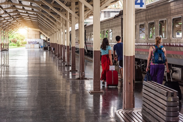 Reizigerstoeristen lopen en slepen bagage om de trein te nemen op het treinstation