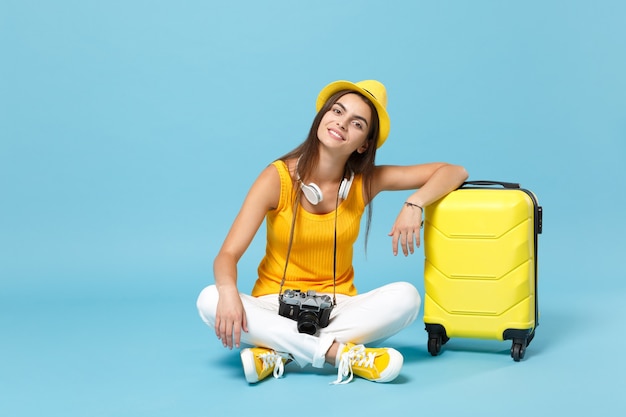 Reizigerstoeristenvrouw in gele vrijetijdskleding, hoed met kofferfotocamera op blauw