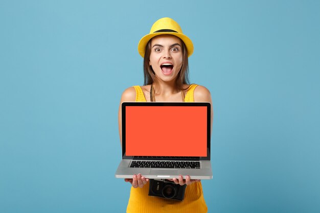 Reizigerstoeristenvrouw in gele zomerkleren, hoed met laptop pc-computer op blauw