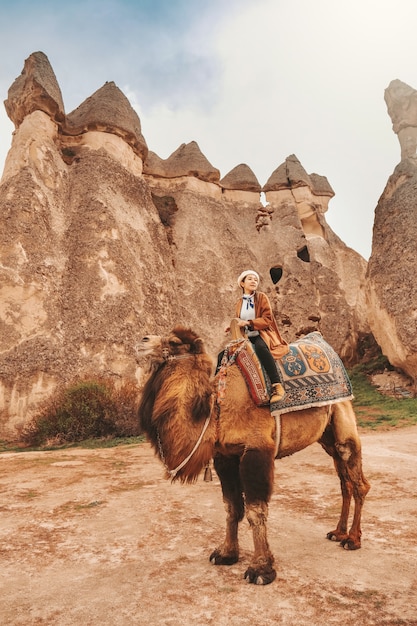 Foto reizigersvrouw berijdende kameel bij goreme-feeschoorstenen, cappadocia.