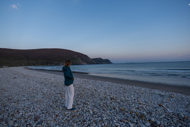 Reizigersvrouw die zonsondergang op rotsachtig strand bewonderen