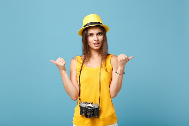 Reizigersvrouw in gele zomerse vrijetijdskleding en hoed met fotocamera op blauw