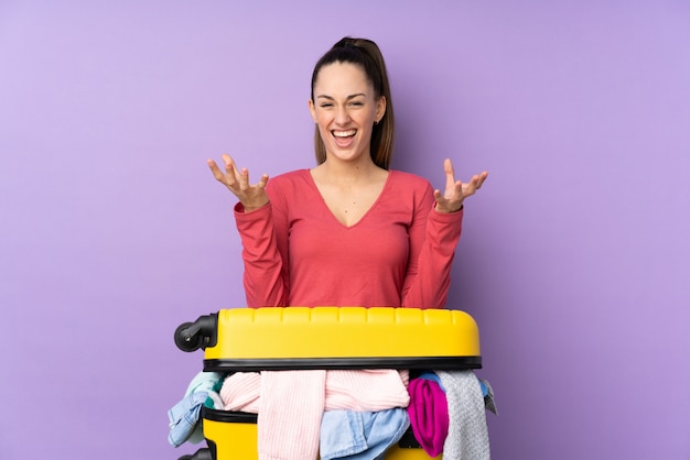 Reizigersvrouw met een koffer vol kleren over geïsoleerde purpere muur ongelukkig en gefrustreerd met iets