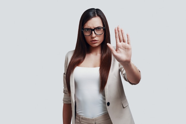 Rejection. Attractive young woman looking at camera and gesturing while standing against grey background