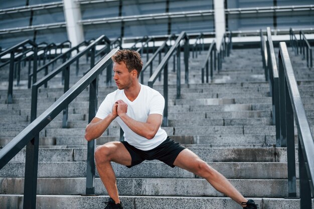 Rekken en voorbereiden Jonge man in sportieve kleding traint overdag buiten