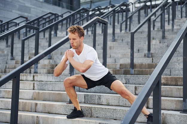 Rekken en voorbereiden Jonge man in sportieve kleding traint overdag buiten