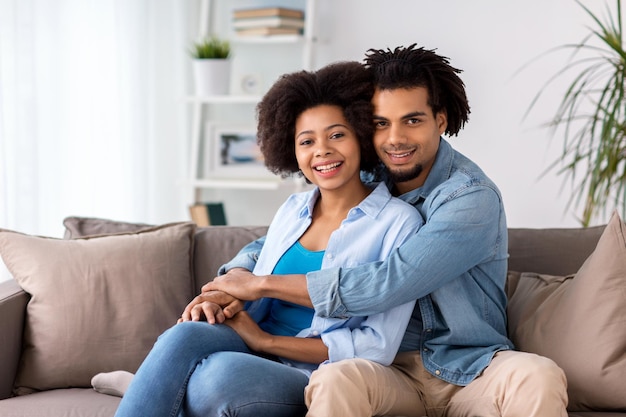 relations, communication and people concept - happy couple sitting on sofa and hugging at home