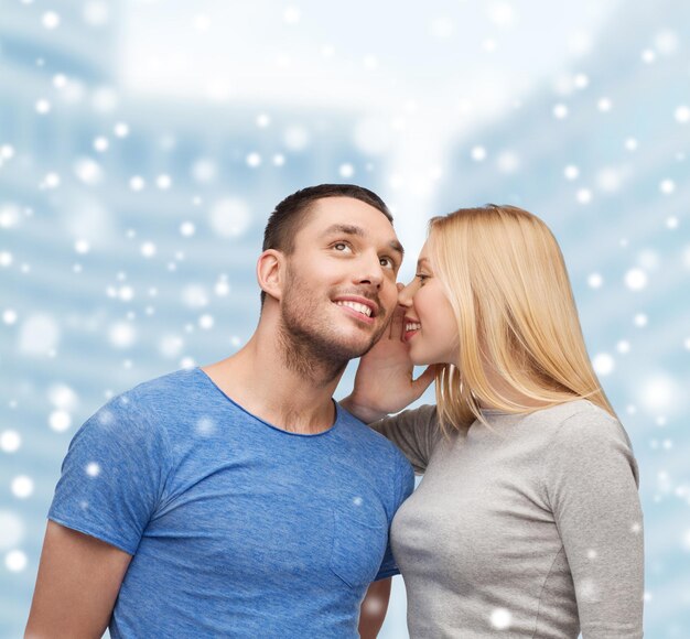 relationships, love, people, information and couple concept - smiling girlfriend telling boyfriend secret over snow and city buildings background