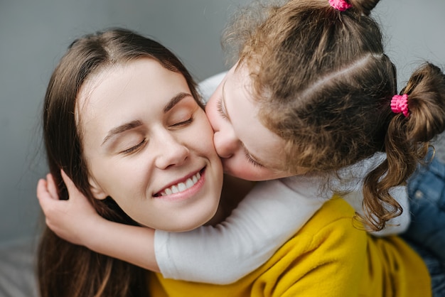 相対的な人々の家族の概念。かわいい愛らしい面白い子供娘の自宅のベッドで遊んで頬若いママにキス、母親や乳母の残りを取る笑顔、小さな女の子はお母さんと一緒に優しい瞬間を楽しむ、愛