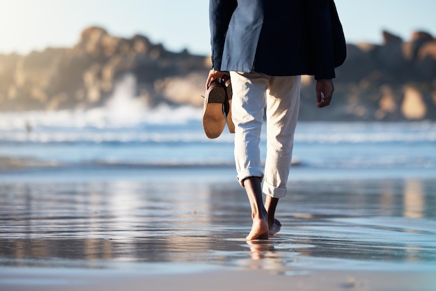 Relax beach and man walking with shoes in hand for peace travel and wellness on vacation Health travel or summer with feet of guy step in the sand for calm nature and lifestyle on Brazil holiday