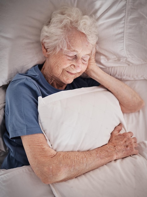 Relax bedroom and old woman sleeping in peace resting in a house or home dreaming with a soft pillow in hand Bedding healthy grandmother or tired elderly person in retirement enjoys napping alone