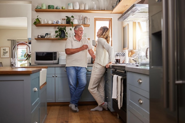 Relax coffee and elderly couple in a kitchen bonding and talking in their home together Love woman and mature man enjoying retirement and relationship indoors casual conversation in the morning