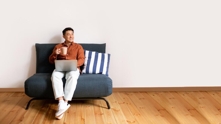 快適なソファに座って夢を見ているPCを使ってコーヒーを飲むコンセプトの幸せなアジア人男性をリラックス