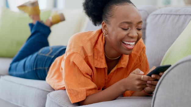 Relax funny phone meme or black woman on sofa in communication in house living room Smile scroll or happy African lady on couch laughing texting or reading online gossip on mobile app discussion