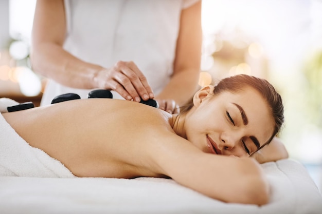 Relax hot stone and woman getting a back massage at a spa for luxury calm and natural self care Beauty body care and tranquil female person sleeping while doing a rock body treatment at a salon