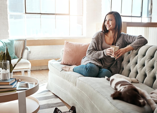 Relax morning tea and woman with dog on a home living room couch feeling calm with happy lifestyle Happiness and smile of person with puppy thinking with coffee on peaceful lounge day in a house
