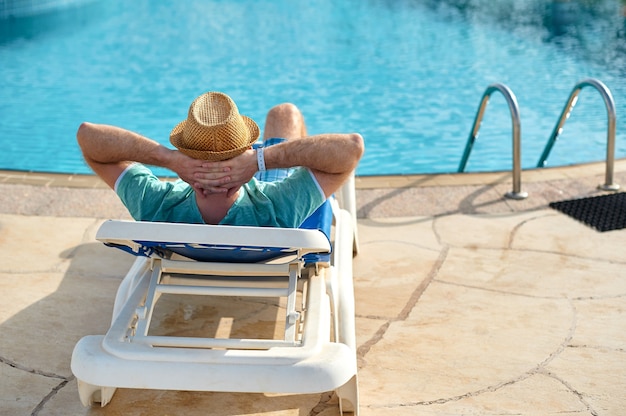 Отдыхайте в бассейне летом. Молодой и успешный мужчина лежит на шезлонге в отеле.