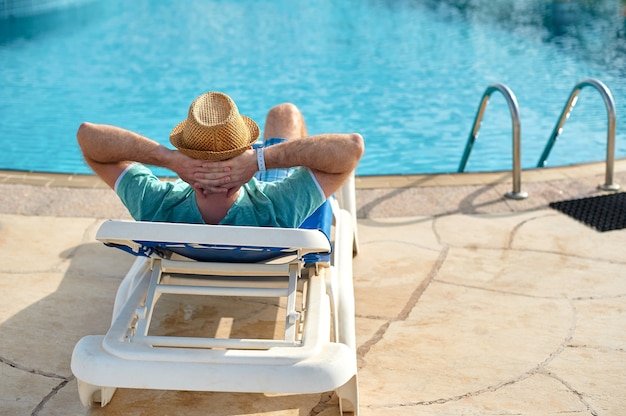 夏のプールでおくつろぎください。ホテルのサンラウンジャーに横たわっている若くて成功した男。