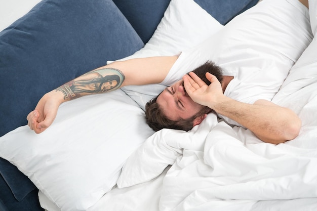 Relax and sleep concept man bearded guy sleep on white sheets\
healthy sleep and wellbeing man bearded hipster sleepy in bed early\
morning hours insomnia and sleep problems lets start new day