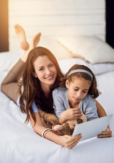 タブレットと母親と子供と寝室でリラックスアプリインターネットまたはソーシャルメディアでオンラインビデオを見るベッドでデジタルテクノロジーでストリーミング映画映画またはショーを少女と一緒に笑顔を愛し
