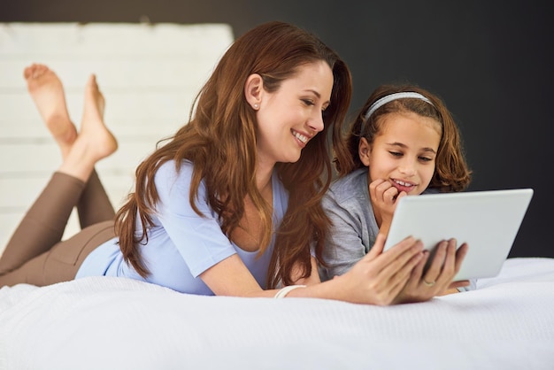 タブレットとママと子供を寝かせてリラックスアプリインターネットまたはソーシャルメディアでオンラインビデオを見る恋とママの笑顔女の子とストリーミング映画映画または寝室でデジタル技術のショー