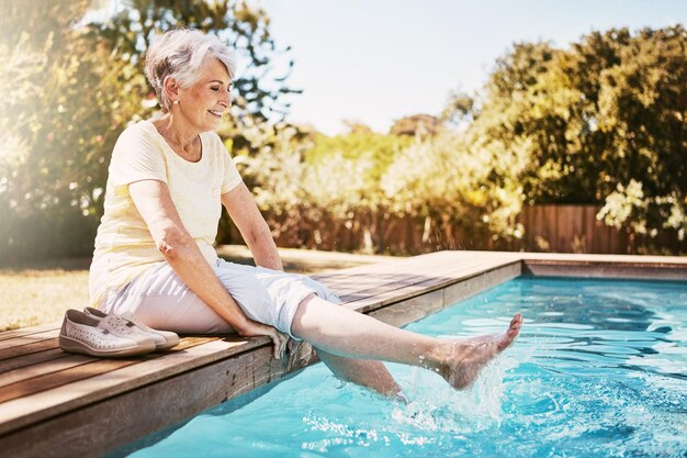 Расслабьтесь в путешествии и пожилая женщина у бассейна во время отпуска или поездки на свежем воздухе летом Счастливая улыбка и пожилая женщина на пенсии с ногами в бассейне на курорте