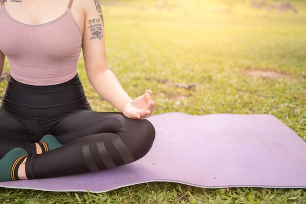 Relaxation exercises Cropped shot of a woman practicing yoga in the morning outdoors sitting in lotus pose and meditating in the park