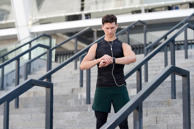 Relaxation exercises. Runner looking at wearable sports watch. checking pulse on watches. fit man checking time. Young Sporty Male With Fit Body In Sportswear Using Fitness Tracker.