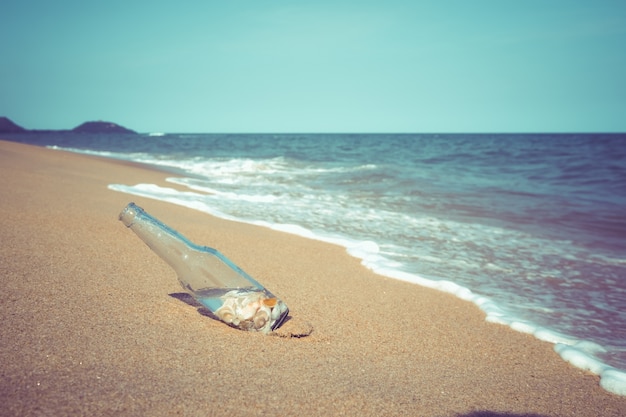 Photo relaxation and leisure in summer - bottle with seashell at tropical beach in summer. vintage color tone effect