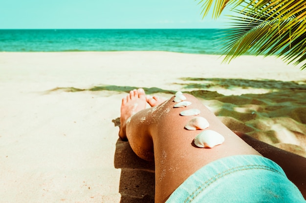 Relaxation and Leisure in summer - Seashell on tanned girl leg at tropical beach in summer. vintage color tone