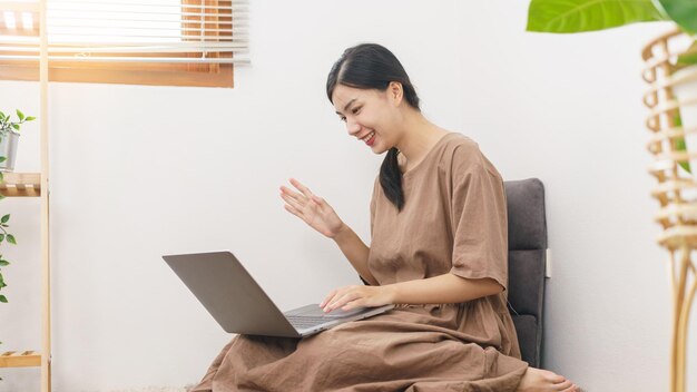 Relaxation lifestyle concept Young Asian woman use laptop to video call with friend in living room