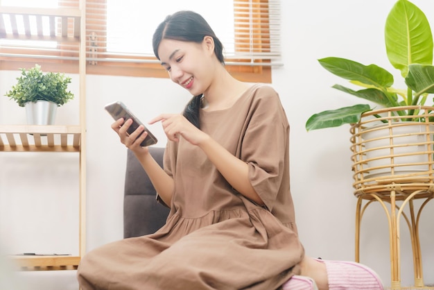 Relaxation lifestyle concept Young Asian woman use smartphone to surf social media in living room