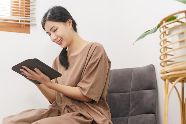 휴식 생활 방식 개념 거실에 앉아 태블릿에 글을 쓰는 젊은 아시아 여성
