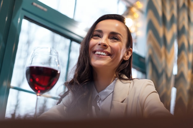 Relaxation method. Low angle of happy jolly gay woman posing with glass of wine while laughing and looking straight