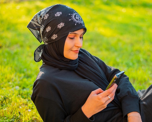 Relaxation with a mobile Break time Young Muslim woman using cellphone and sitting on the grass