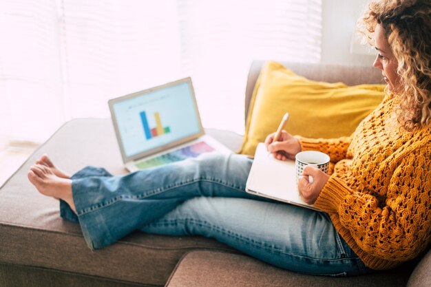 Relaxed adult caucasian woman at work at home with personal laptop computer and notebook 