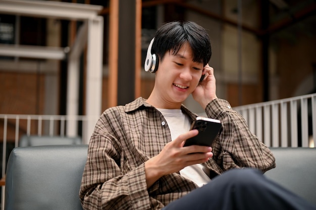 リラックスしたアジア人男性がスマートフォンを使い、ヘッドフォンで音楽を聴いている