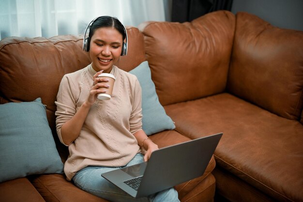 Relaxed asian woman enjoy listening to music through her\
headphones while working from home