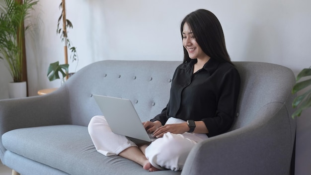 Relaxed asian woman enjoying her weekend surfing internet on laptop at home