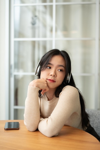 A relaxed Asian woman hand on her chin and listening to music or online podcast on her headphones