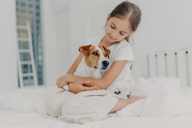 Relaxed beautiful small girl plays with pedigree dog, embraces favourite animal