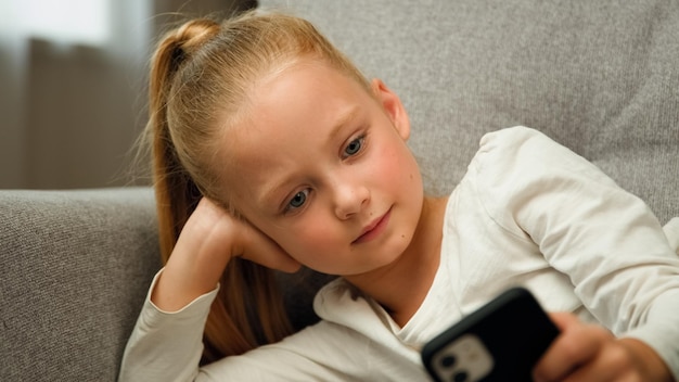 Relaxed blonde child little girl blogger cute kid teen resting on couch playing online games on