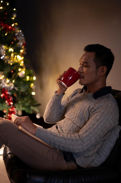 Relaxed and calm Asian man enjoying his coffee or hot cocoa in a living room on his Christmas night