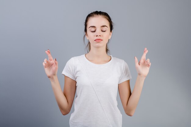 Relaxed calm young woman praying holding fingers crossed isolated over grey