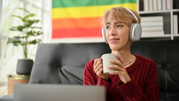 편안하고 조잡한 젊은 아시아 게이 남자가 음악을 들으면서 커피를 즐기고 있습니다.