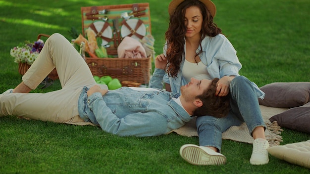 Расслабленная пара проводит время на пикнике Очаровательный мужчина лежит на ноге женщины на одеяле в зеленом законе Красивая девушка гладит волосы парня на романтических свиданиях в парке, а молодые люди разговаривают на природе